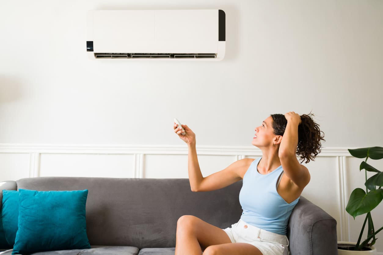 An adult woman sitting uncomfortably on her couch due to her AC unit blowing warm air