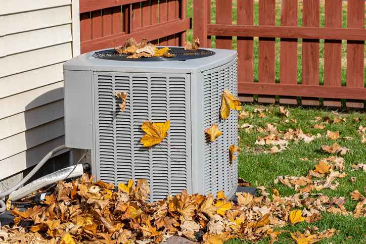 Outdoor HVAC unit covered in and surrounded by leaves during fall.