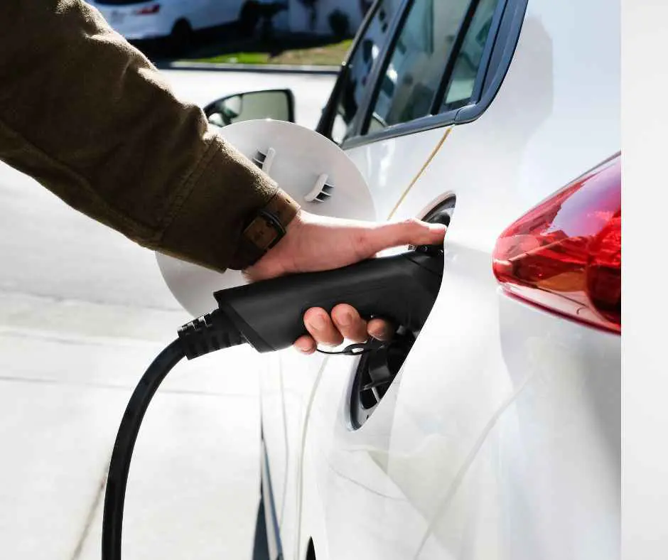 Hand of man inserting a power cord into an electric car for charging ecofriendly vehicle on green landscape