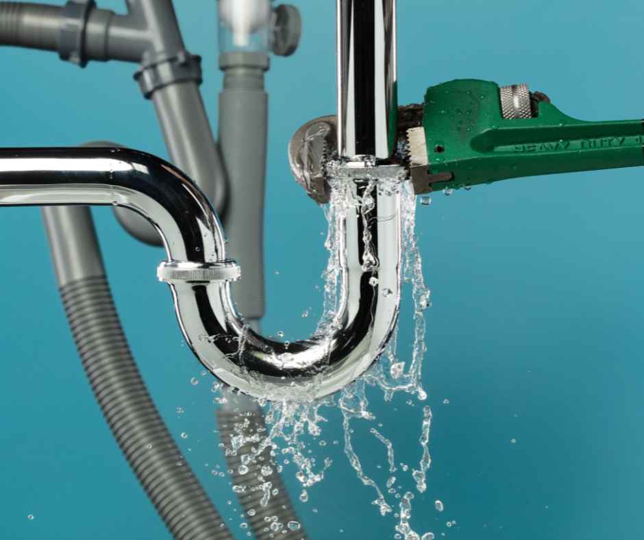 Chrome P-trap being worked on with a green pipe wrench as water leaks from the joint underneath a sink, suggesting a plumbing repair.